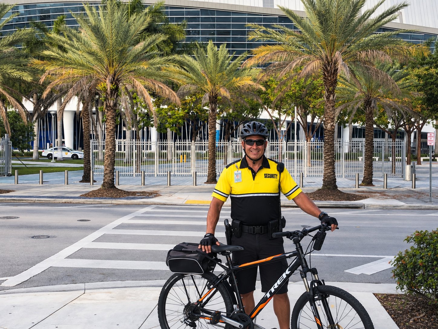A Security Alliance bike patrol officer in a high-visibility uniform standing with a patrol bicycle at a street crossing