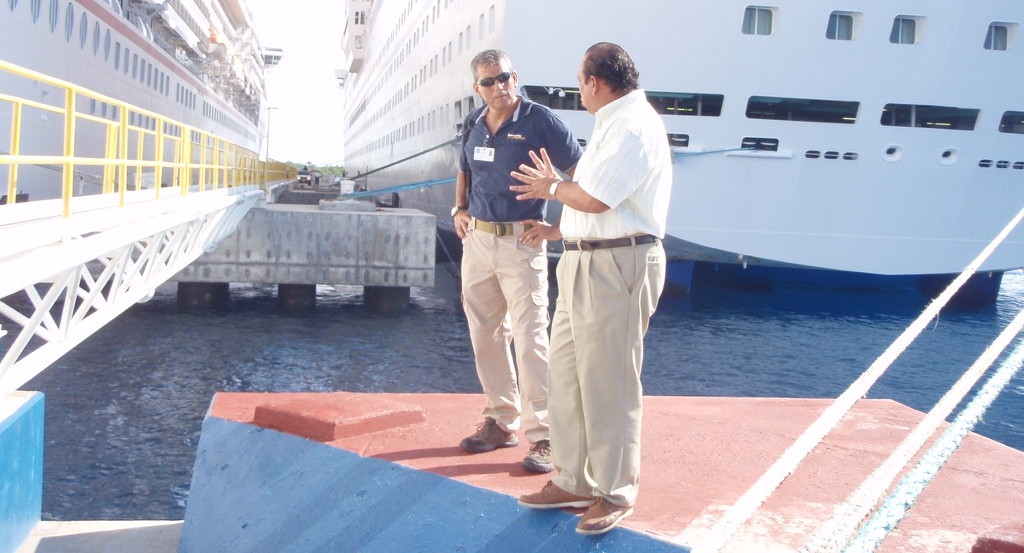 Two Security Alliance personnel conferring on the pier at a cruise terminal, alongside a moored cruise ship and its passenger gangway
