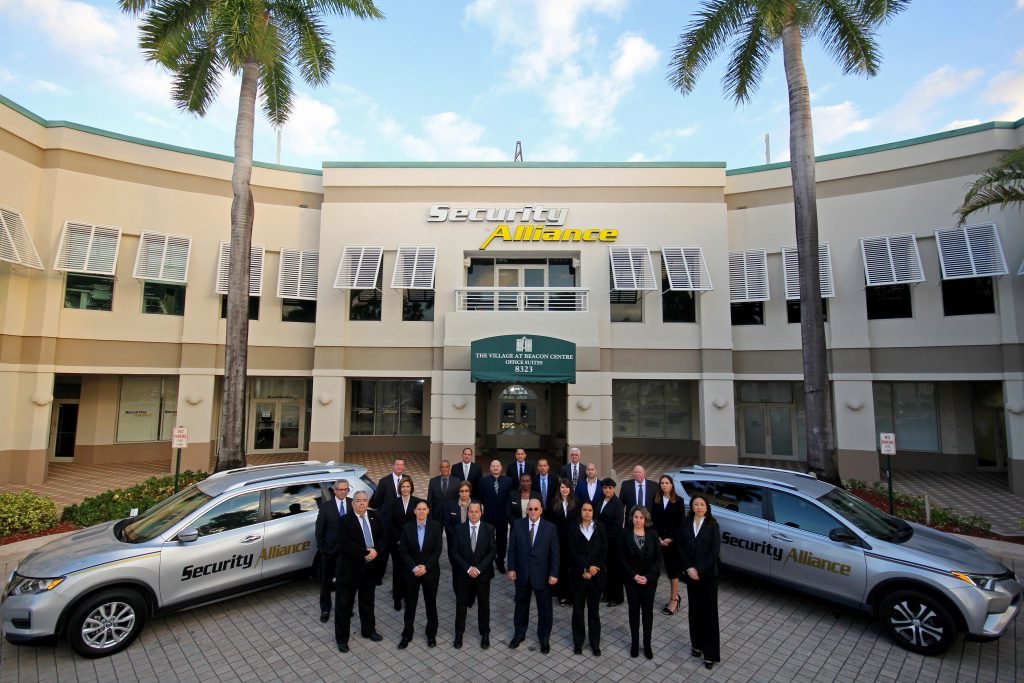 Security Alliance leadership and management team with branded patrol vehicles at the Miami headquarters